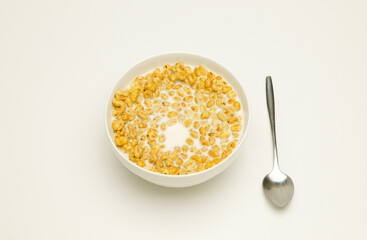 wheat flakes with milk in a white cup and tablespoon on a white background