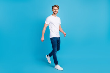 Fototapeta na wymiar Full length portrait of satisfied man walking beaming smile look camera isolated on blue color background
