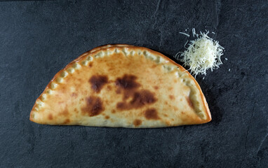 pie or closed pizza with cheese on a dark gray stone background