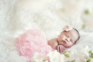 Newborn girl with chubby cheek with little hand wearing a pink tutu and cherry blossom hairband Lying on a soft, white carpet surrounded by flowers 