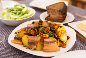 baked potatoes with chanterelles and bacon served with herbs and lightly salted cucumbers on table