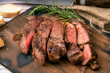 Churrasco of meat cut into pieces on a wooden board in a rustic setting. Close up.