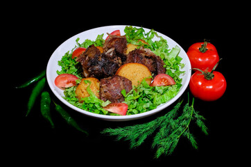 fried meat with potatoes, greens, hot pepper and tomatoes on a black background