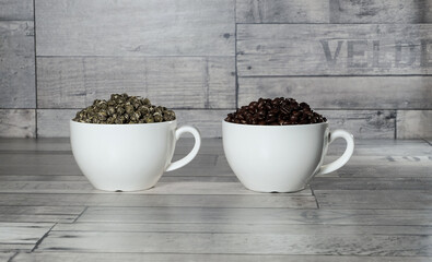 black coffee in beans and green leaf tea in white cups on a coarse wooden gray background