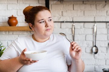 Sad pensive obese fat young woman eating flakes for breakfast. Starving caucasian plus size woman dieting for being in good shape