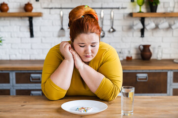 Sad hungry fat obese woman with a plate full of pills and medicine for losing weight. Healthy dieting, bad eating habits concept - obrazy, fototapety, plakaty
