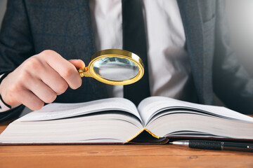 a man examines a book with a magnifying glass - obrazy, fototapety, plakaty