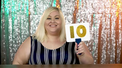 A glamorous shot of a woman reality show judge evaluating the talent of a contestant with a "10" number palette.  	