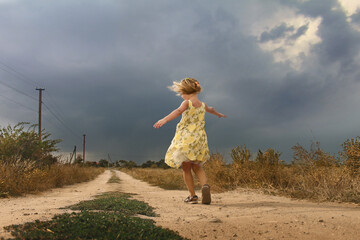 A little girl in a yellow dress walks along the road after a thunderstorm.