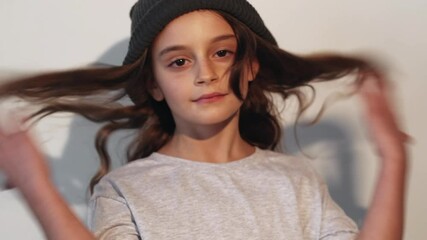 Kid fashion. Street style look. Carefree childhood. Confident preteen girl with cute face in casual outfit knitted hat walking by posing isolated on light neutral background loop.