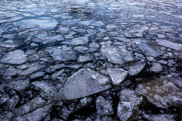 Broken ice of dark blue color on the river. Chunks of crushed ice on dark water. Abstract ice background. Blue background with cracks on the ice surface. Cracks of frozen water