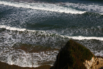 Waves reach to coastline that surrounded with rocks.