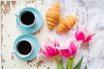 nice cup of coffee, croissants and pink tulips on old white table, close-up