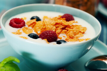 Breakfast of cornflakes and raspberries, blueberries and milk in a blue plate