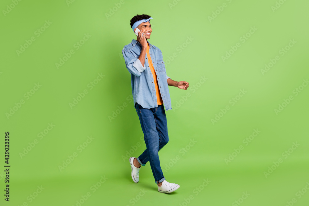 Sticker Full size profile photo of optimistic nice brunet guy go talk telephone wear band shirt jeans sneakers isolated on green background