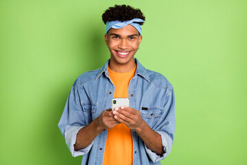 Photo of guy hold telephone beaming smile wear headband jeans shirt footwear isolated green color background