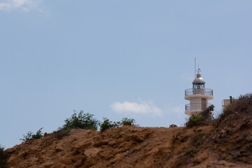 Cabo de las Huertas Lighthouse, in Alicante, behind a hill next to the coast.