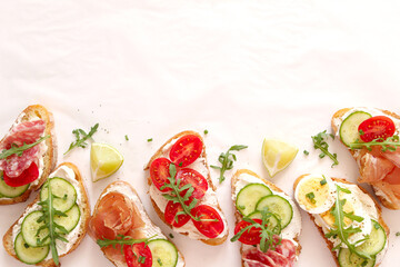 Variety of sandwiches with light cheese, vegetables and salami on light background. Top view.