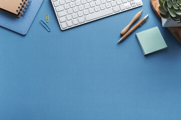 Blue desk with keyboard blank note, supplies. Stylish home office workspace. Overhead view. - obrazy, fototapety, plakaty