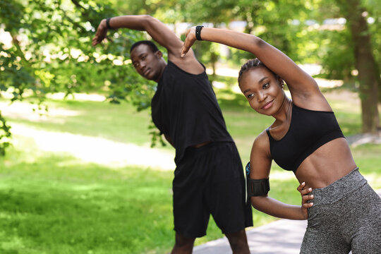 Sporty African Couple Doing Fitness Workout Together In Summer Park, Stretching Muscles