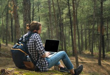 Naklejka na ściany i meble Man sitting on ground at forest talking on smartphone and working on laptop