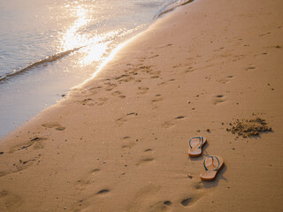Summer vacation concept from orange flip flops on sandy beach during sunset, soft focus lens flare sunlight.