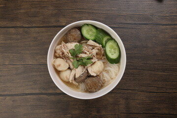 Clear white rice vermicelli beehoon noodle soup with chicken beef meat ball shredded cucumber in white bowl chopsticks spoon chili soya sauce parsley garnish