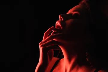 rote beleuchtung auf sexy frau, die lippen lokalisiert auf schwarz berührt. © LIGHTFIELD STUDIOS