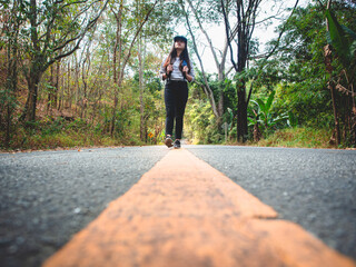 Woman hiking with backpack walking on roadway amid greenery trees. Girl are happy and cheerful while traveling.