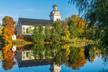 Fototapeta premium White church by a river in Sweden surrounded by autumn colored trees
