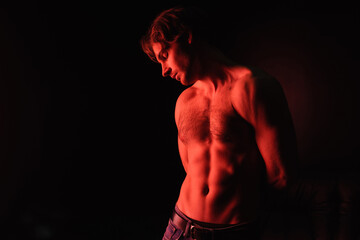 Fototapeta na wymiar red lighting on body of sexy muscular man standing isolated on black.