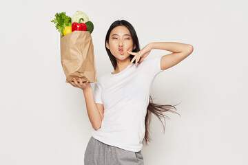 woman with a package of groceries on a light background and a white t-shirt gesticulate with her hands