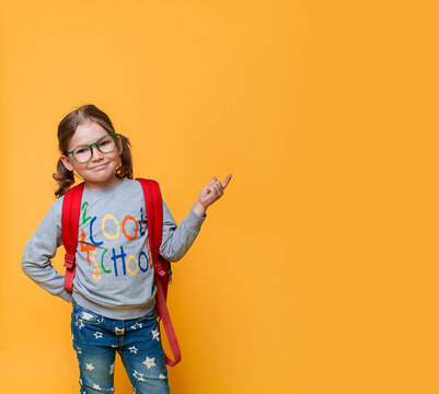 Back To School. Too Cool For School. Education, School And Virtual Screen Concept. Little Girl Pointing Up Isolated On Yellow. Kid In Eyeglasses And With Backpack