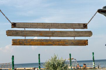 Vintage wooden plank signs on the chains near the beach bar. Old wood signboard with metal chain and three planks at coast.