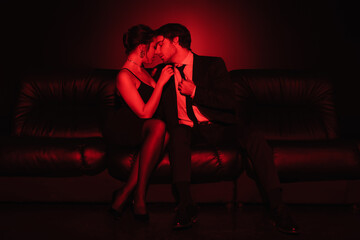 red lighting on sexy couple hugging on black leather sofa.