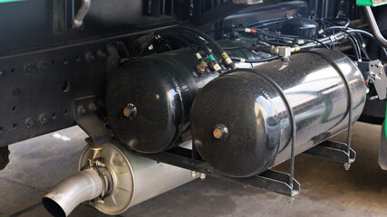 Black air tank for truck brake system. Brass fittings with air breeze on the dirty twin cylinders on the racks of large trucks. On a cement patio background with a copy space. Selective focus