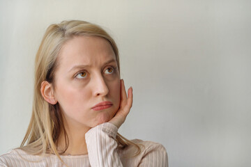 portrait of thinking or dreaming blonde girl on grey background. Space for text. Banner. the girl holds her chin in her hand