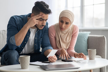 Confusded lady in hijab and her upset husband with bills