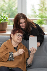 Senior woman and her granddaughter using modern gadget. A teenage girl and grandmother with tablet at home.