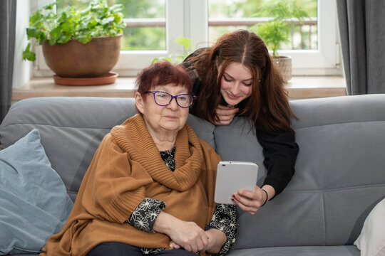 Senior woman and her granddaughter using modern gadget. A teenage girl and grandmother with tablet at home.
