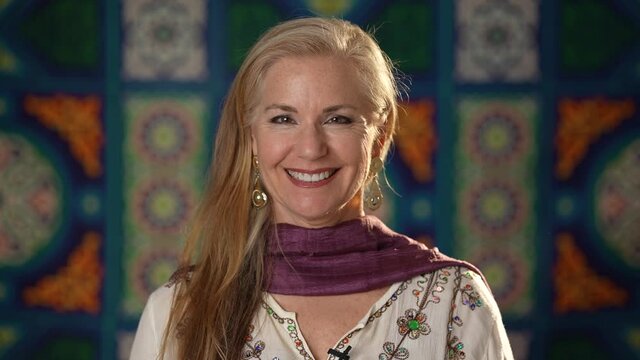 Closeup portrait of a pretty blond haired woman happy smiling looking at camera wearing ethnic clothes on ethnic arabic or Turkish background. Happy mature woman enjoys life.
