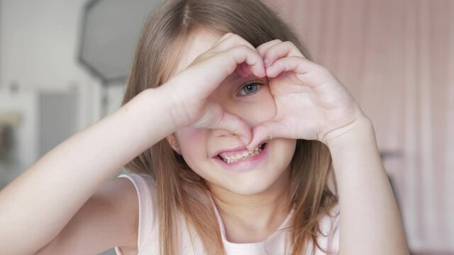 Smiling cute little girl kid showing hands sign heart shape looking at camera. Healthy heart health life insurance, love and charity, voluntary social work, organ donation concept, close up portrait