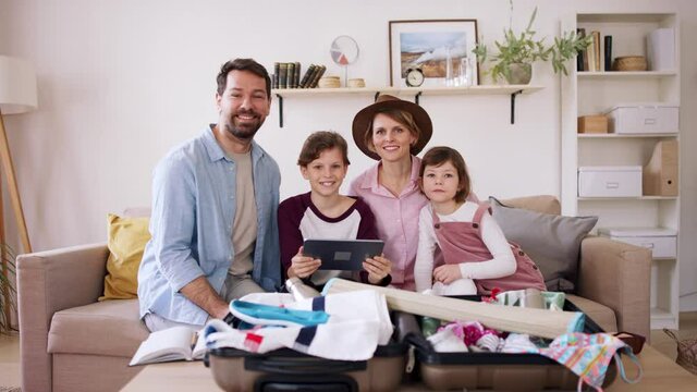 Beautiful family packing, making preparations for vacation on tablet and looking at camera.