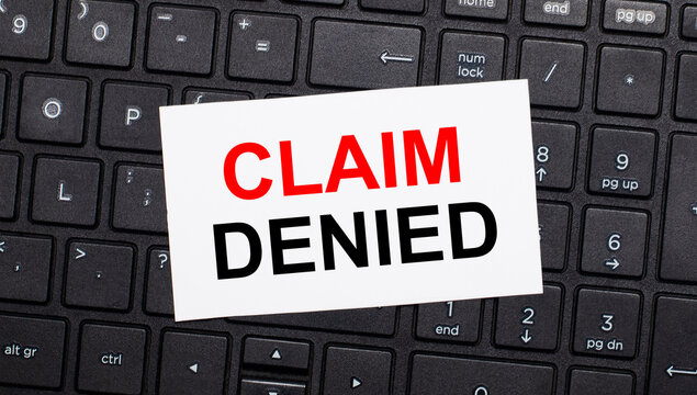 On a black computer keyboard there is a white card with the text CLAIM DENIED. View from above