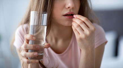 Unrecognizable young lady holding glass of water, taking pill at home, panorama