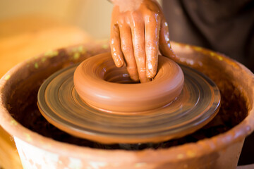 Hands of potte makes pottery dishes on potter's wheel. Sculptor in workshop makes clay product closeup