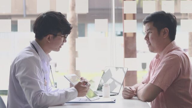 Young Asian man in a white robe talks to a man, Doctors diagnose diseases and give advice or treatment solutions to patients in the hospital examination room, Explaining medical examination results.