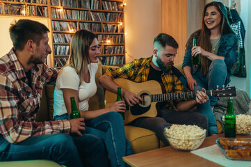 A group of friends playing guitar and drinking beer at home