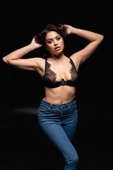 Fototapeta na wymiar young brunette woman in lace bra and jeans looking at camera on black.