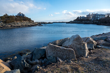 a wide angle view of a rocky coast with a lake, mansions, and a bright blue sky in the background 